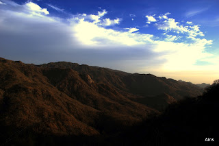 "A stunning morning view of Mount Abu, with overcast skies, silhouettes of trees and hills in the foreground, and distant mountains and clouds visible in the background."