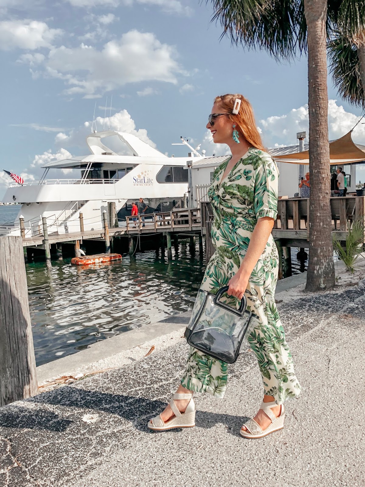 tampa blogger affordable by amanda wearing a yellow and green palm print jumpsuit from bealls outlet. she is walking in front of the starlite cruise ship. she is holding a clear bag from Target and wearing platform tommy hilfiger espadrilles from bealls outlet. 