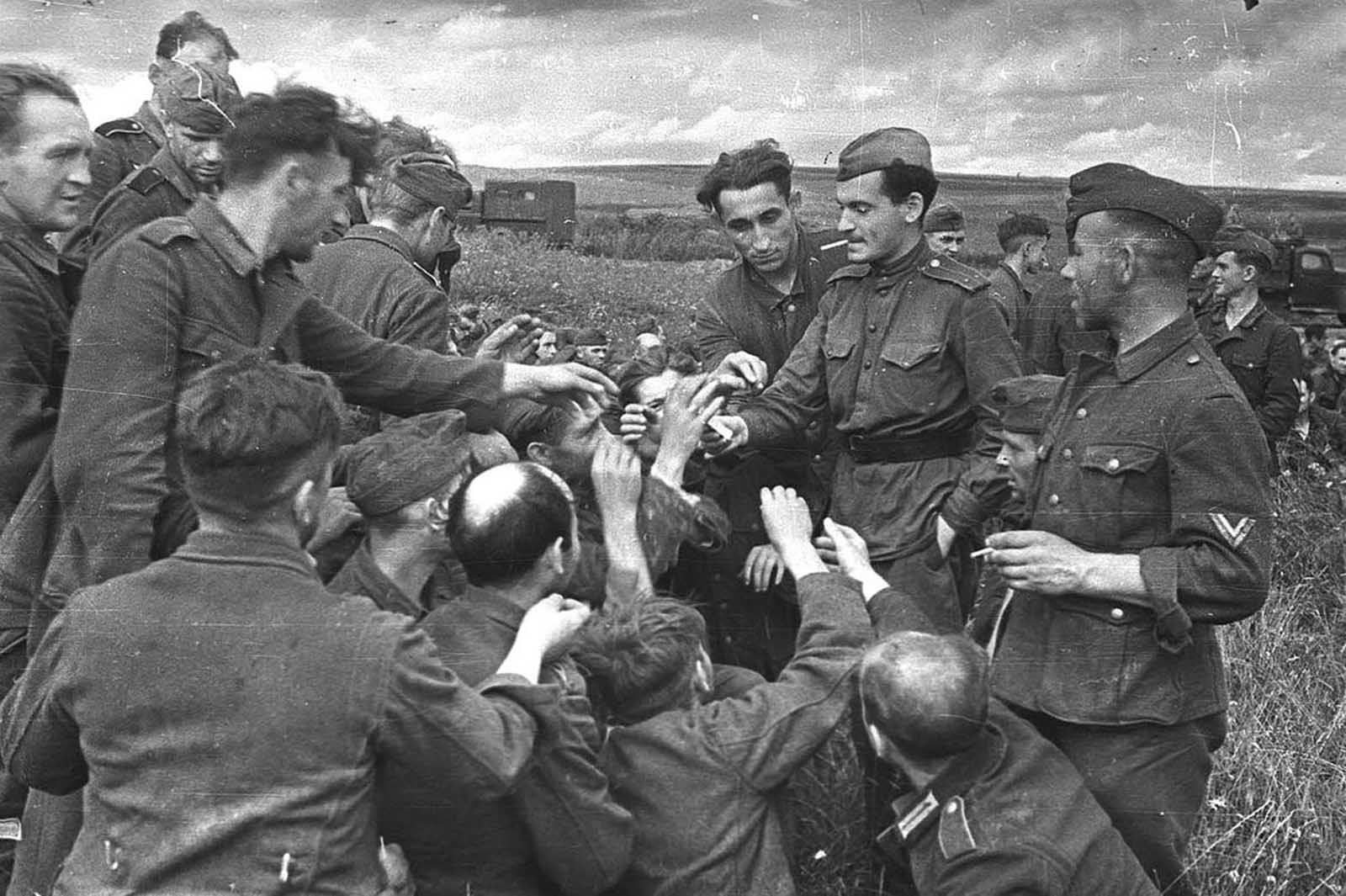 A Soviet lieutenant hands cigarettes to German prisoners somewhere near Kursk, in July of 1943.