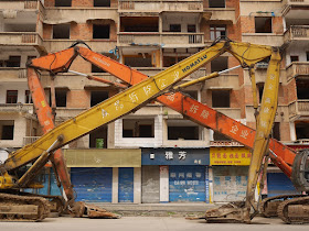 two large construction vehicles parked forming a symmetrical pattern with their arms