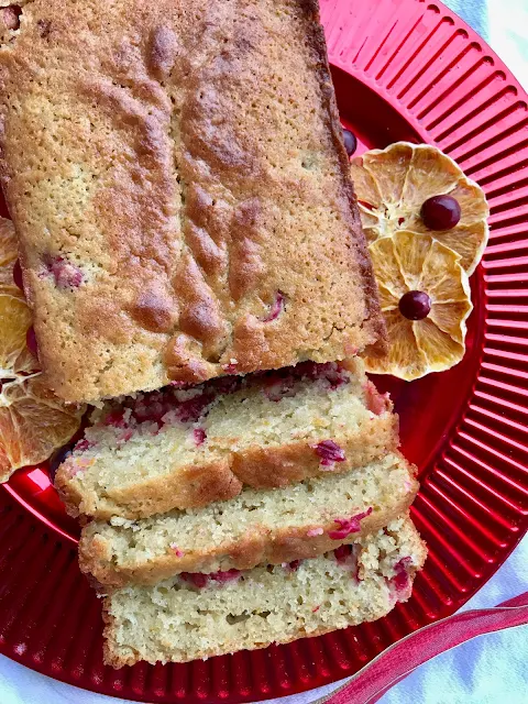 Finished loaf of cranberry orange bread on a plate with a few pieces sliced.
