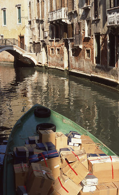 boxes in green boat floating down Venetian canal.