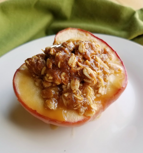 The perfect individual sized dessert, these mini apple crisp baked apples are the perfect mix of baked apples and crisp topping. Serve it with a scoop of ice cream for a perfect dessert! close up of an apple half transformed into a mini apple crisp baked apple with a drizzle of caramel sauce