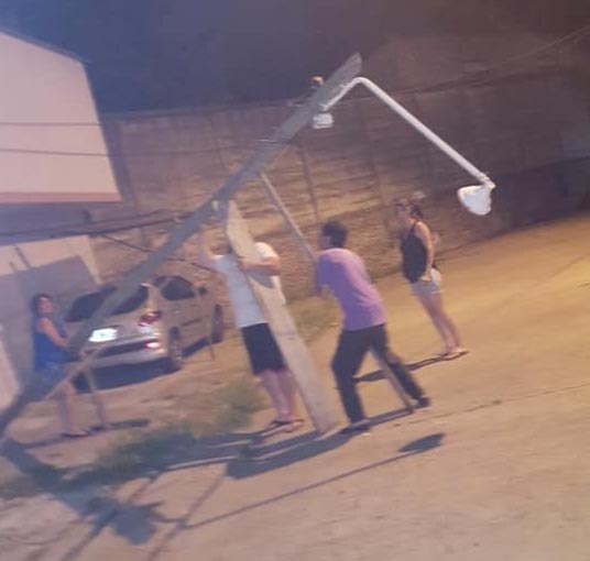 Vecinos sostienen un poste de luz con una escalera y palos para que no se  caiga