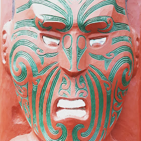 Close up of a maori carving of a face, painted in red and green.