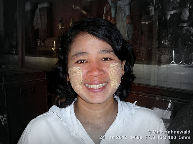 Closeup focal black-and-white street portrait (head shot, full-face view) of a smiling Burmese woman, wearing traditional thanaka face cosmetic,; Bagan, Myanmar. Burma; Myanmar; Bagan; Burmese woman; people; portrait; focal black and white; thanaka; Facing the World; eye contact; smiling; Burmese face cosmetic; yellowish-white cosmetic paste; travel; headshot; Matt Hahnewald Photography; ethnic; ethnic portrait; posing; 4 : 3 aspect ratio; photo; image; travel portrait; environmental portrait; culture; one person; real people; human; photography; consent; empathy; rapport; portraiture; travel destination; tourism; horizontal format; world cultures; human face; human eyes; closeup; street; post-processing; editing; experiment; Photoshop; Picasa; focal B&W; experimental; amazing; interesting; inspirational; educational; facial expression