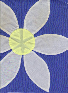 Appliqué of a flower on blue background. White petals show through yellow center.