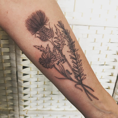 Steph's tattoo on her left forearm it's a black thistle, daisy and a sprig of rosemary