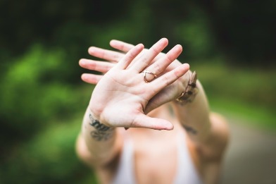 A photo of a woman taken from an angle above her. Her arms are outstretched to the camera, her hands crossing, blocking her face from view. The photo is focused on her hands, everything else is blurry.