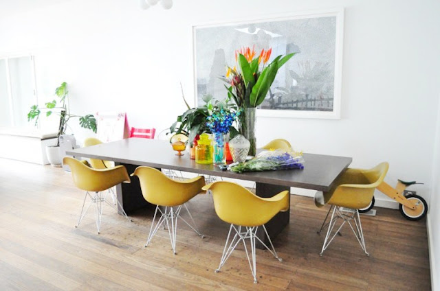 Dining room with wood floors, yellow Eames chairs around a modern dark wood table