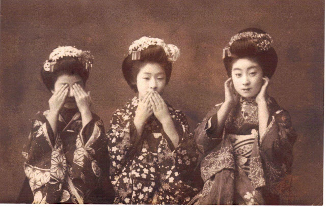 Cepia toned photograph which A Japanese post card from the late 19th century, which shows three geisha imitating the Three Wise Monkeys. Left to right they are: Mizaru (see no evil), Iwazaru (speak no evil), and Kikazaru (hear no evil).