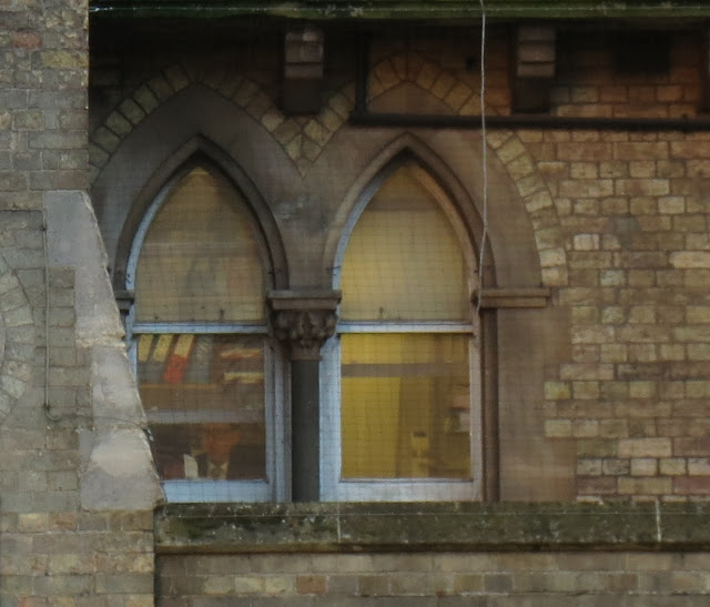 Man reading letter in office with files. Seen through window in pale brick building.