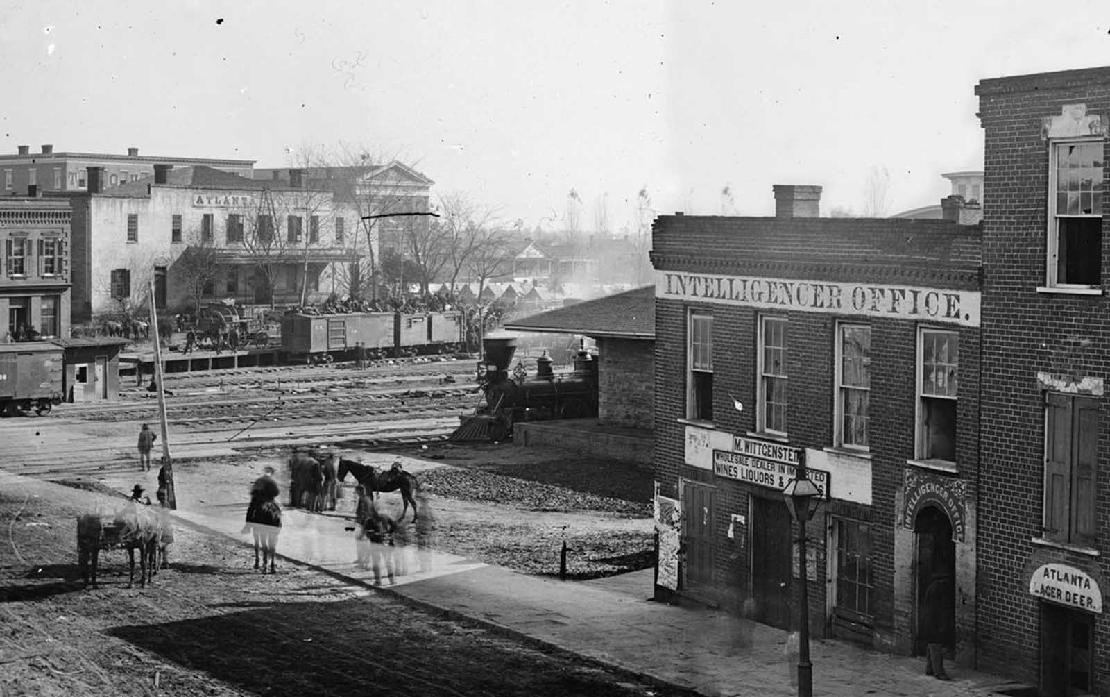 In Atlanta, Georgia, soldiers sit atop boxcars at a railroad depot. At right is the office of Atlanta's Daily Intelligencer newspaper. Panorama made from two photographs taken by George N. Barnard in 1864.