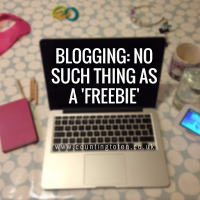 Title text of "Blogging: No such thing as a 'freebie'" over a blurred background showing a laptop on a table surrounded with various clutter of family life