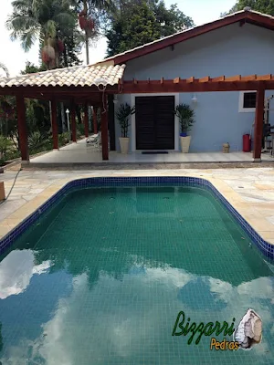 Construção de piscina em residência em condomínio em Atibaia-SP com o piso de pedra São Tomé e o pergolado de madeira.