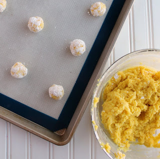 bowl of lemon cookie dough with ball of dough rolled in powdered sugar on baking sheet