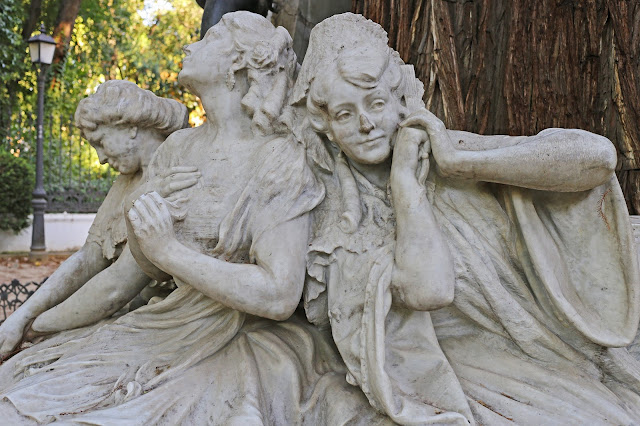 Tres estatuas femeninas sentadas bajo un árbol del parque.