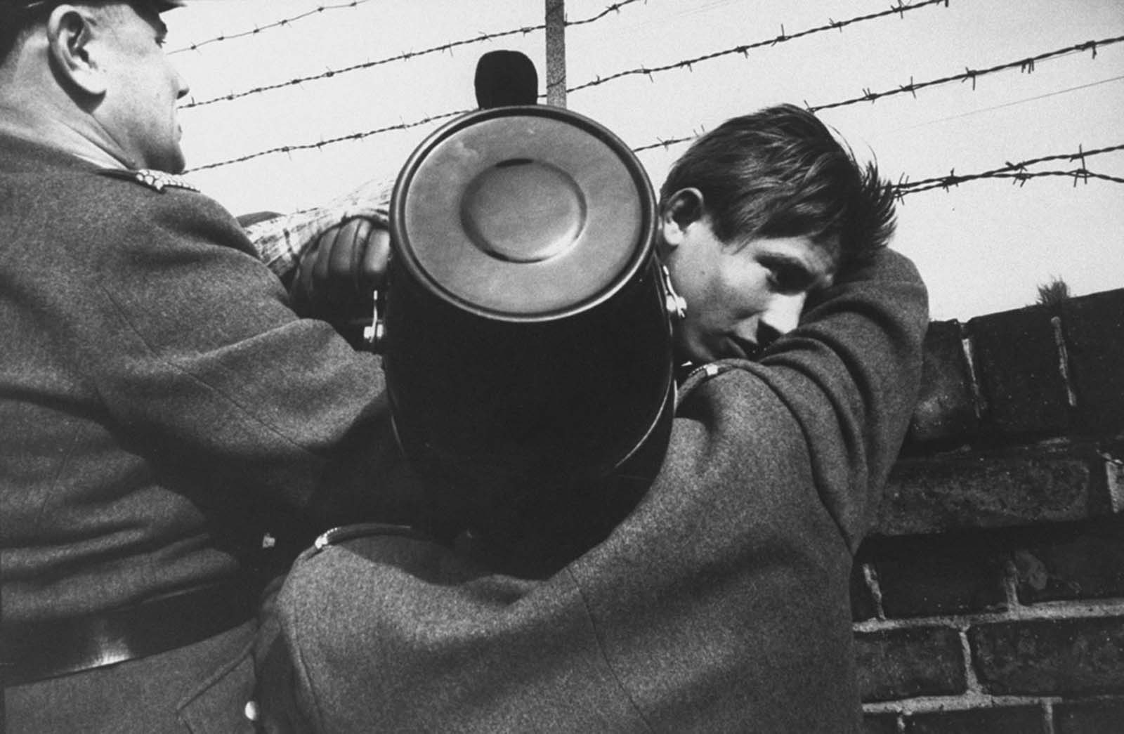 Egy 17 éves keleti berlini ifjúságot két barátságos nyugat-berlini rendőr segít lefelé a berlini falról, miután 1961 októberében szabadon mászott.