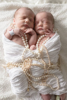picture of newborn twin girls wrapped in a white scarf with strands of pearls draped cutely over them