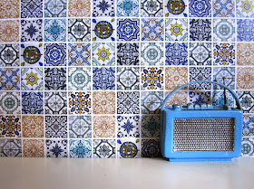 Modern dolls house miniature tiled wall in a selection of blue and white tiles. In front of it is a miniature Roberts radio in blue.