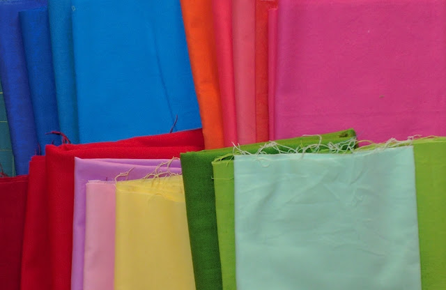 Solid fabric choices for the hourglass quilt A rainbow array of solid fabrics in two rows.