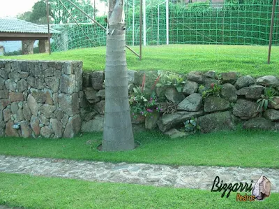 Pedra moledo na execução do paisagismo com o muro de pedra para formar o platô do campo de futebol com grama esmeralda.