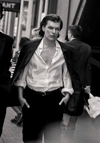 Actress Milla Jovovich looking stern, wearing a white shirt and suit coat.