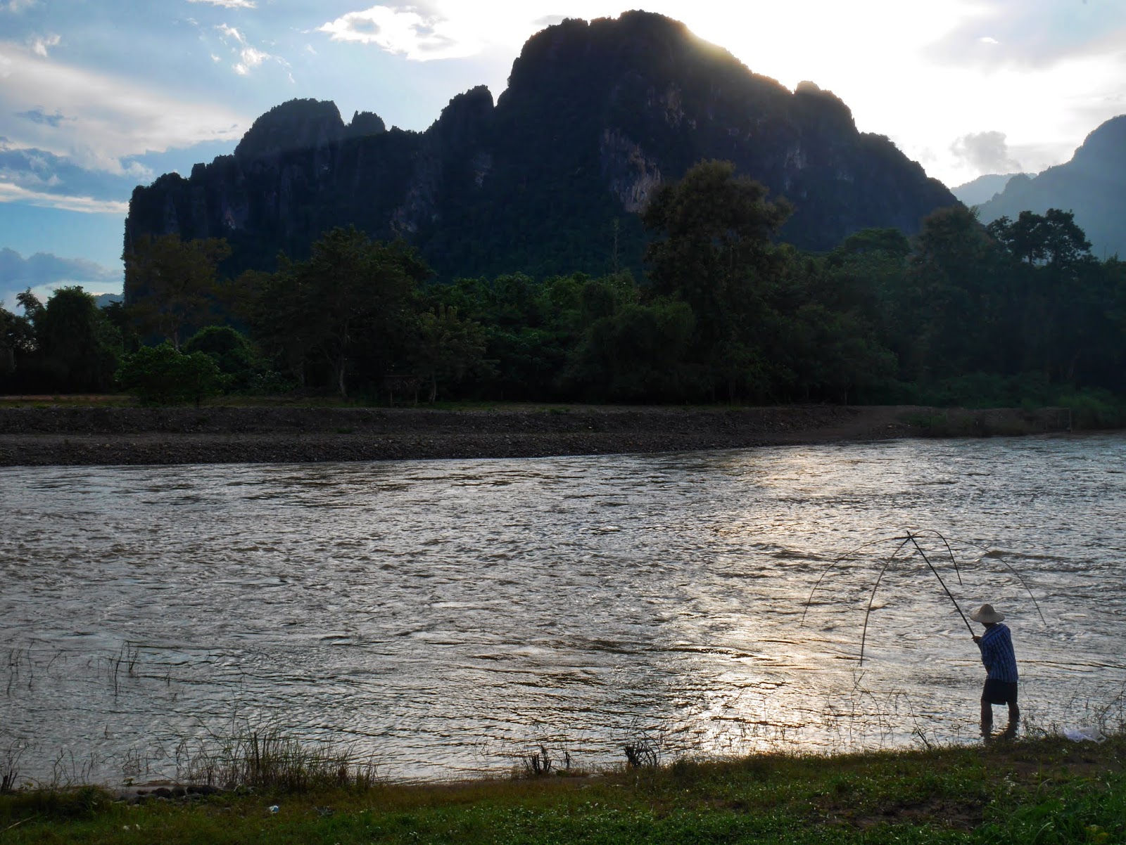fisherman a local fisherman catching fish with a net as the sun sets over the river with the mountains in the background, vang vieng, laos