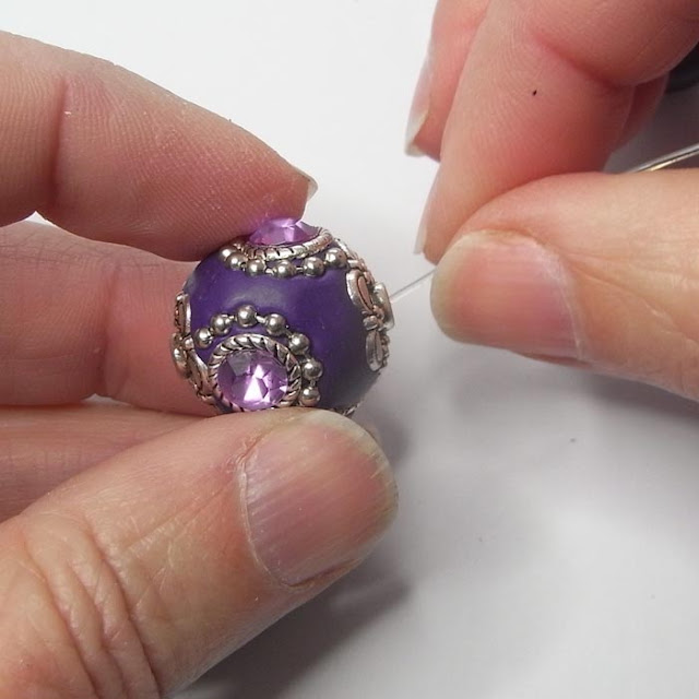 Large purple Kashmiri bead being strung on beading elastic