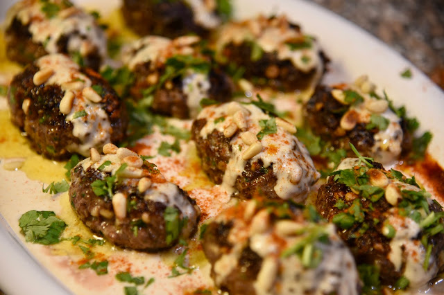 Kofta drizzled with tahini sauce and butter and sprinkled with parsley, pine nuts and paprika