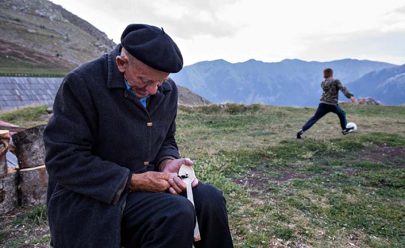 A man makes wooden spoons while a boy plays ball.