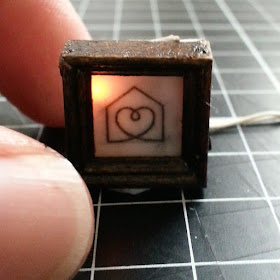 Tiny one-twelfth scale framed sketch of a heart in a house, with a light behind the sketch.