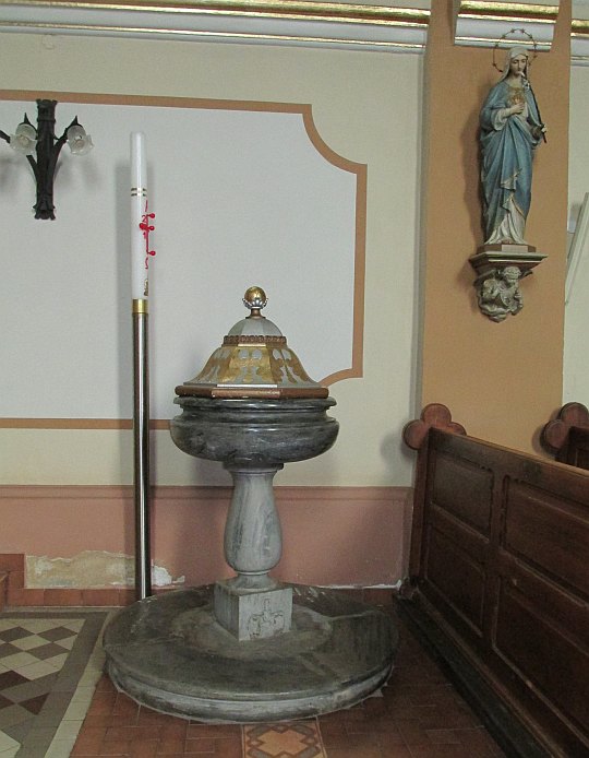 Marmurowa chrzcielnica z kartuszem herbowym zachowana z poprzedniej świątyni. Marmurowa chrzcielnica z kartuszem herbowym zachowana z poprzedniej świątyni.