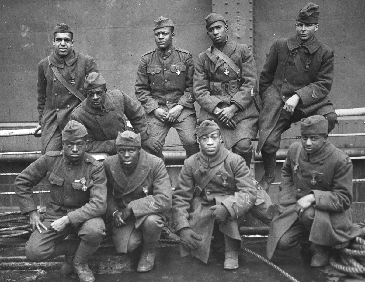 Original caption: Some of the colored men of the 369th (15th, NY) who won the Croix de Guerre for gallantry in action. Front row, left-to-right: Private Eagle Eye, Ed Williams; Lamp Light, Herbert Taylor; Private Leon Fraitor; Private Kid Hawk, Ralph Hawkins. Back row, left-to-right: Sgt. H.D. Prinas; Sgt. Dan Storms, Private Kid Woney, Joe Williams; Private 