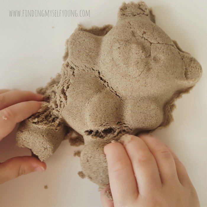 toddler fingers playing with kinetic sand teddy bear mould