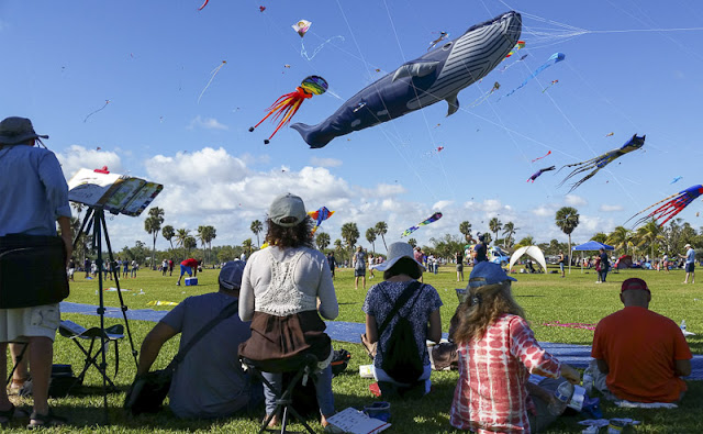 Group of people sitting together sketching the kites in the sky.