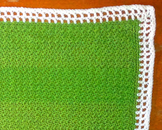 Green blanket crocheted in griddle stitch with a white filet-style crocheted border.