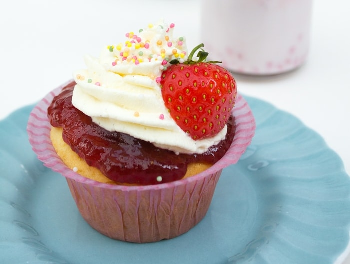 Old-Fashioned Strawberry and Vanilla Fairy Cakes with Sprinkles Close up of Old-Fashioned Strawberry and Vanilla Fairy Cake on a pale blue plate