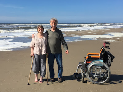 Corina Duyn standing on the beach with her walking sticks beside her brother and her wheelchair