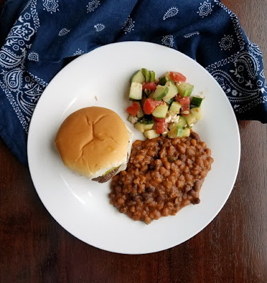 Serve up meaty delicious cowboy beans at your next bbq. They are a hearty and easy to make side dish that is made right in your slow cooker! plate with burger, beans and tomato cucumber salad