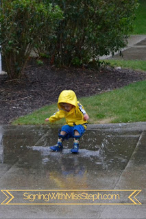 Boy wearing a rain coat and rain boots lands in puddle with a big splah
