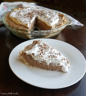 This pie is creamy, luscious, rich and popular every time I make it! Full of chocolaty french silk filling and topped with whipped cream, it is a favorite and so full of memories! slice of french silk pie served on white plate with remaining pie in background