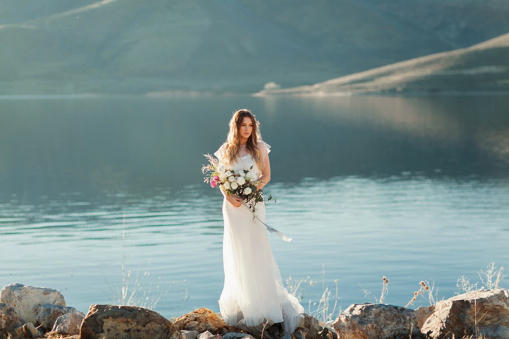 beautiful lakeside bride in a beaded flutter sleeve dress with tallow berry hairpiece and a late winter white and purple bouquet tied with hand dyed soft blue silk and willow ribbon