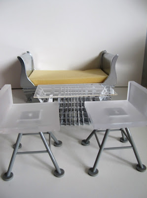 Two modern dolls' house miniature white and grey bar stools from the Kaleidoscope House, a SLICE Tilt coffee table. and a silver sleigh bed.