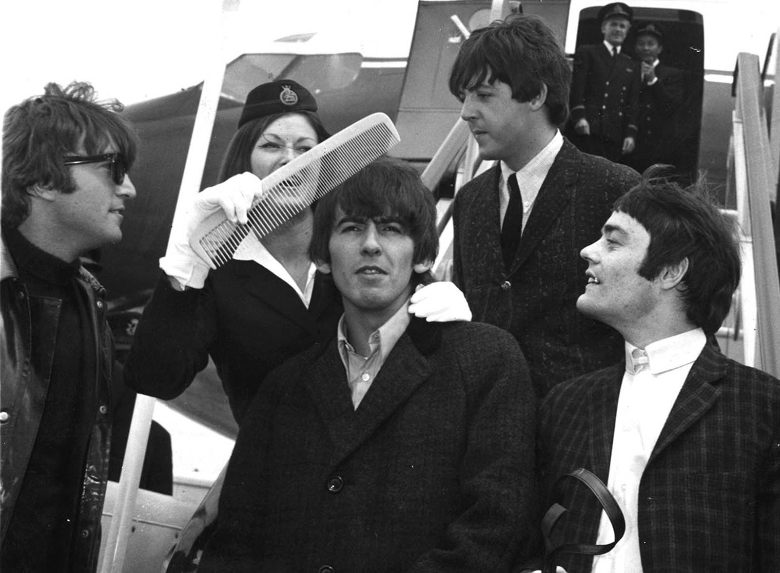 Watched by fellow Beatles, Guitarist George Harrison gets the big comb treatment from BOAC stewardess Anne Creech, after their arrival at Windy airport in London, England, on June 7, 1964. From left: John Lennon, George Harrison, Paul McCartney and drummer Jimmy Nicol, who stood in for Ringo Starr for the trip to The Netherlands.