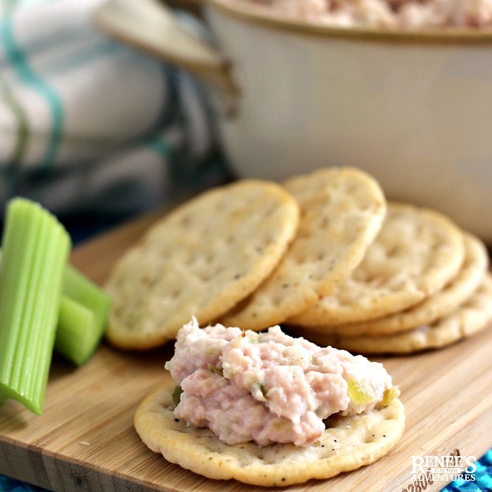 Favorite Ham Salad Recipe by Renee's Kitchen Adventures on a cracker on a wooden board with celery garnish and crackers in the background