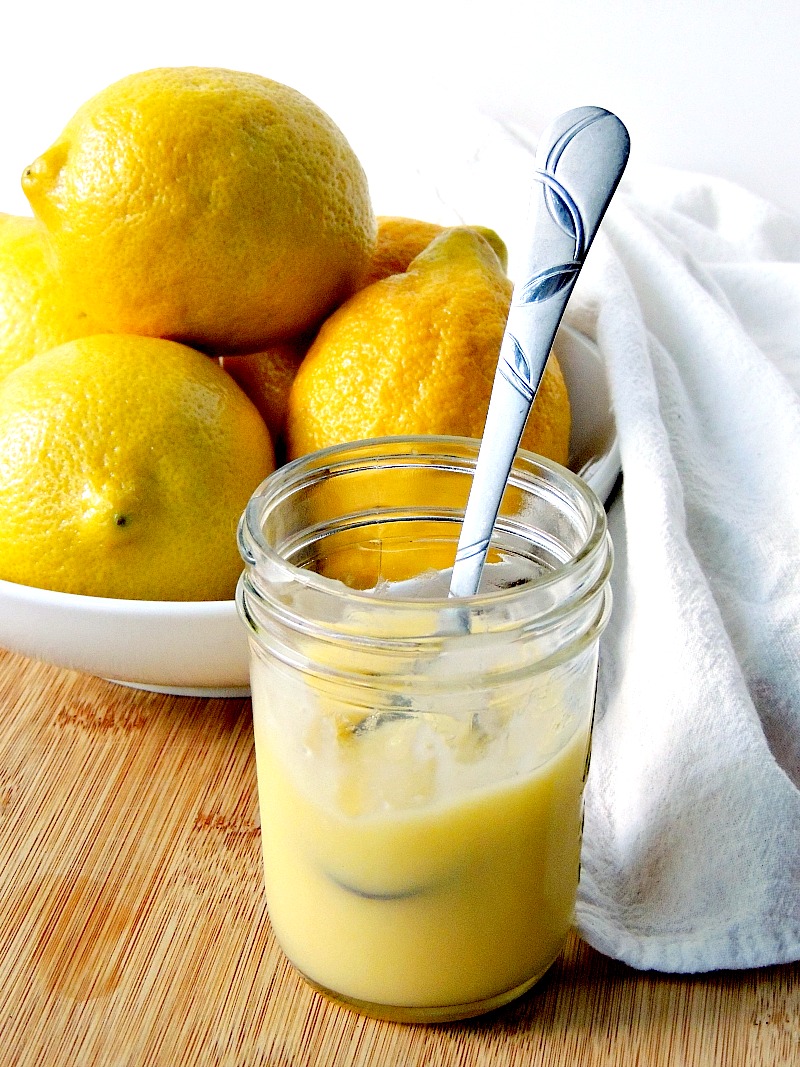 Quick Microwave Lemon Curd in a glass jar with lemons in the background on a wooden cutting board.