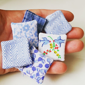 Six unstuffed  dolls' house miniature cushions, in shades of blue and white, on an outstretched hand.