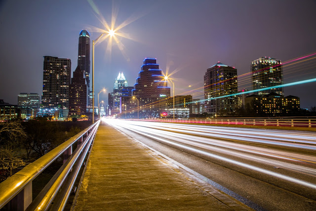 Light trails in a long exposure taken taken of the night time skyline of Austin, Texas as the lights of passing cars stretch into the distance. 