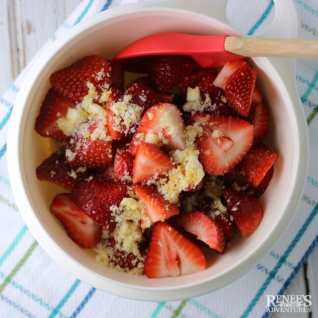 Strawberries and orange sugar in a white bowl with a red spoon ready to be mixed for Strawberries Romanoff | Renee's Kitchen Adventures